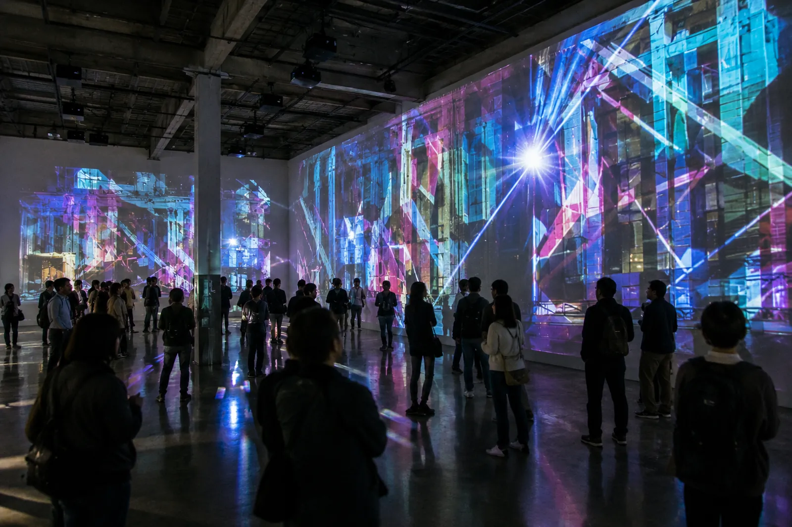 A dark warehouse hall washed in blue and violet projection-mapped light, a crowd silhouetted against the glowing walls.